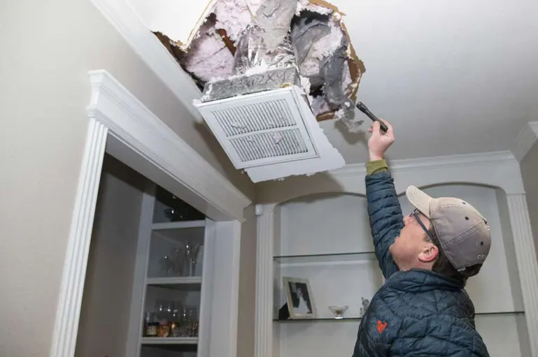 Inspector checking an opened ceiling around a vent for hidden water