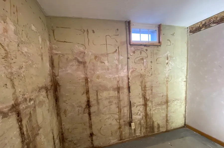 Basement foundation wall streaked with water stains below a small window