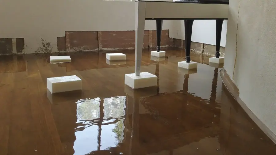 Standing water across a hardwood floor with furniture legs set up on foam blocks